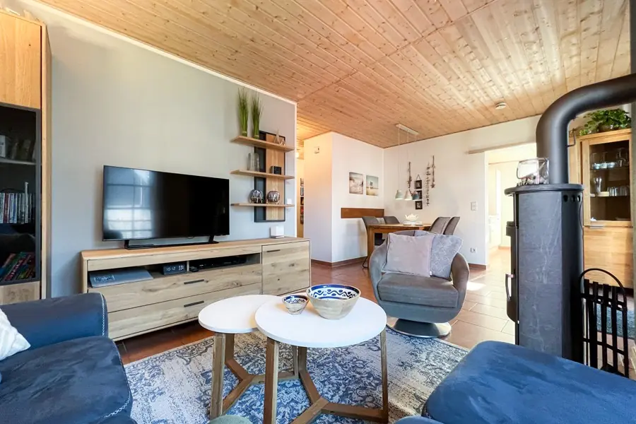 Wohnbereich mit Fernseher, Sofa und Kaminofen, im Hintergrund der Essbereich