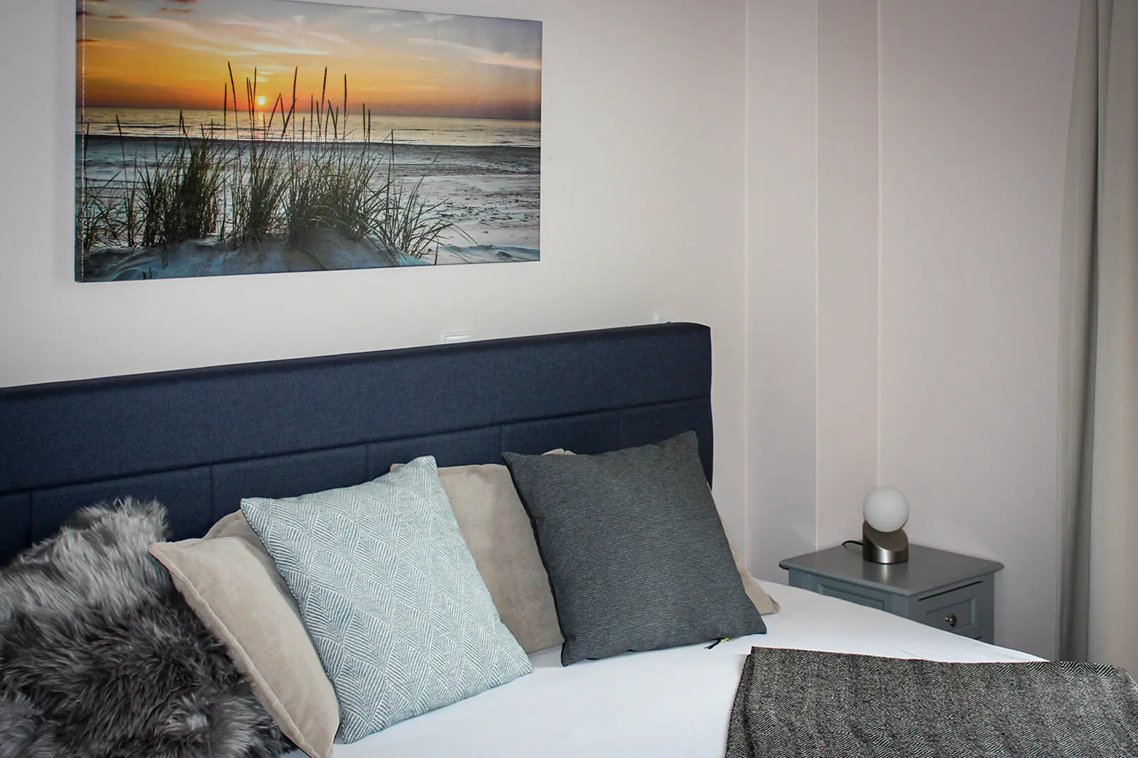 Gemütliches Bett mit Kissen unter einem Strandbild