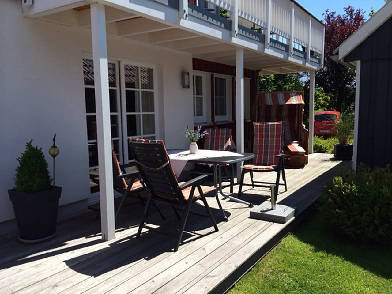 Überdachte Holzterrasse mit Liegestühlen und Strandkorb